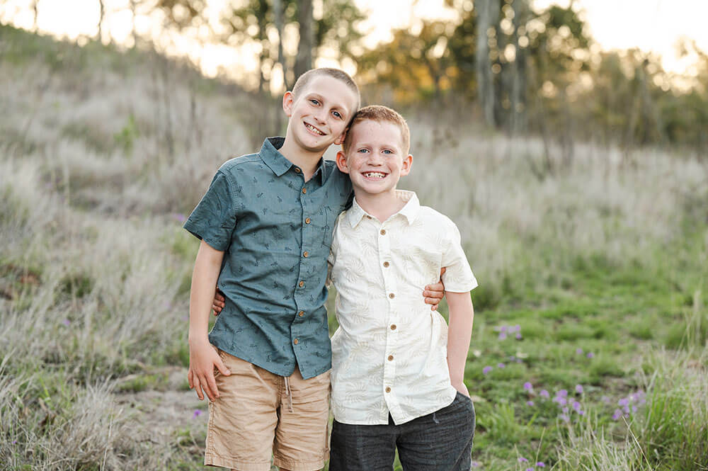 Two brothers stand with their arms around each other for a photo